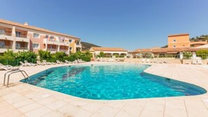 A swimming pool surrounded by lounge chairs and a hotel building with multiple balconies. - Domaine VarAzur by Interhome (Les Issambres)