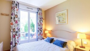 A bedroom with a bed, two bedside lamps, a window with curtains, and a painting on the wall. - Domaine VarAzur by Interhome (Les Issambres)
