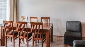 Zona pranzo con tavolo e sedie in legno, lampadario a sospensione e poltrona grigia.