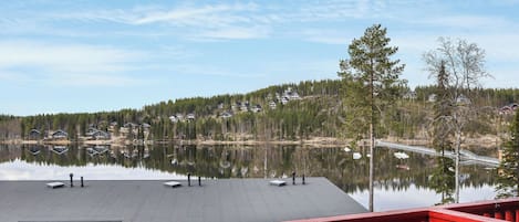 Vista sul lago da un balcone con ringhiera rossa, che si affaccia su un lago calmo e un pendio boscoso.
