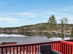A lakeside view from a balcony with a red railing, overlooking a calm lake and a forested hillside. - Skivillas 47 ukkohalla (a7) by Interhome (Hyrynsalmi)