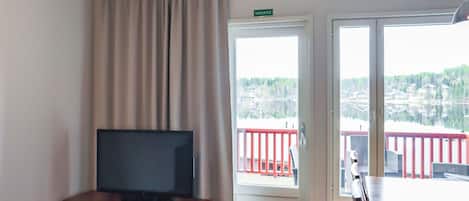 A room with a television on a wooden cabinet, a sliding glass door leading to an outdoor area with a red railing, and a sign above the door reading 'VARATIE'.