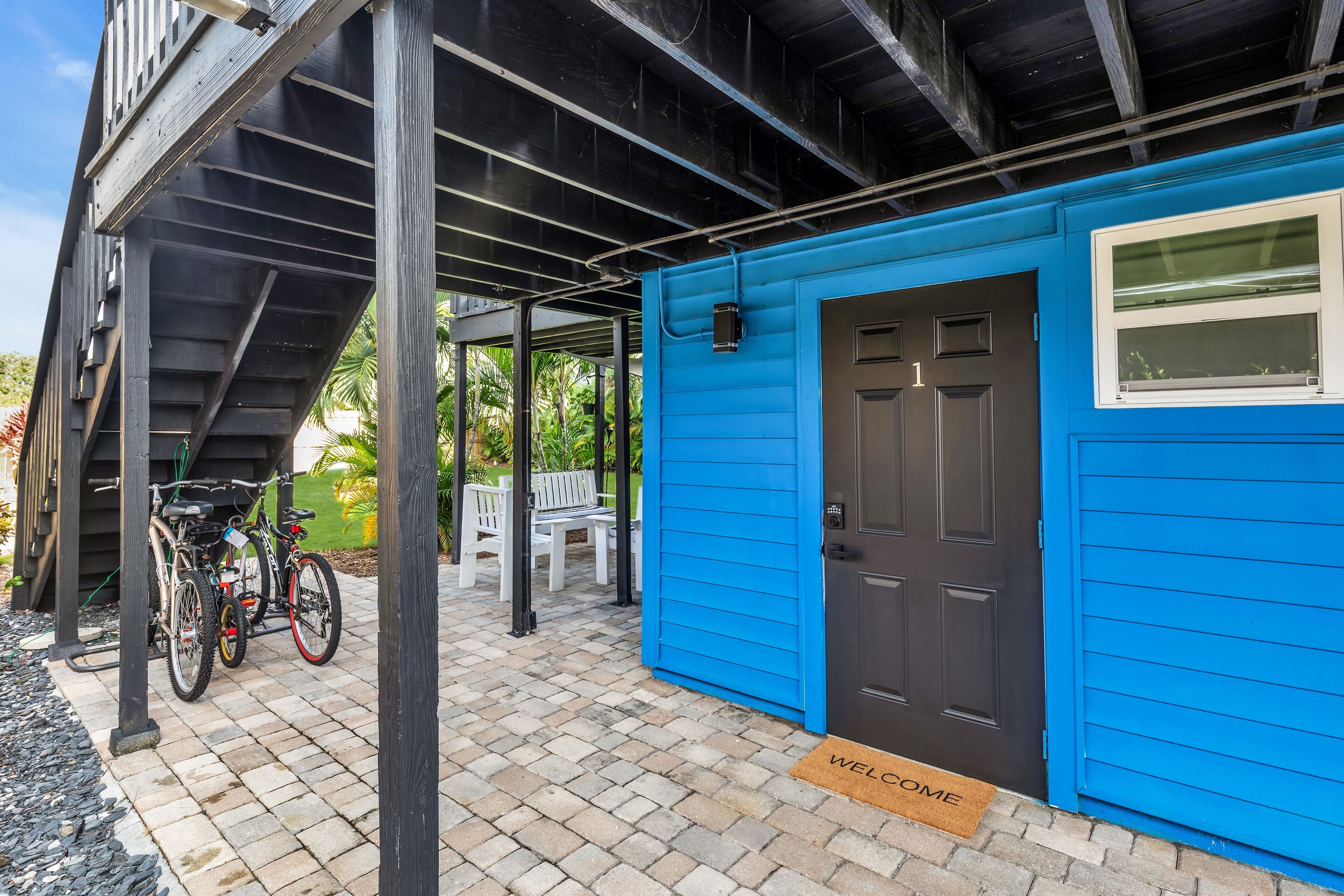 A blue building with a black door and a window, a bicycle parked outside, and a welcome mat on the ground.