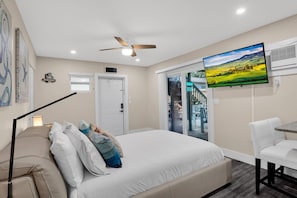 Une chambre à coucher comprenant un lit, un bureau, une chaise, un ventilateur de plafond, une télévision et une porte.