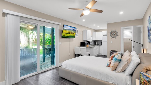 Un dormitorio moderno con una cama grande, ventilador de techo, televisor y puerta corrediza de vidrio que da a un patio.