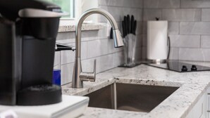 Una cocina con un lavamanos de acero inoxidable, una cafetera y una ventana que ofrece vistas a zonas verdes.
