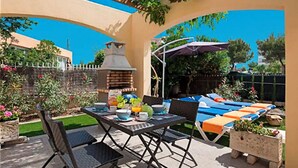 An outdoor patio with a table set for dining, a barbecue grill, and lounge chairs.