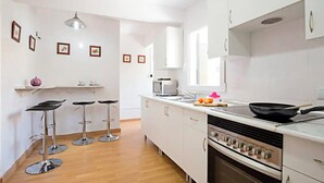A modern kitchen with white cabinets, a stove, a microwave, and three bar stools.