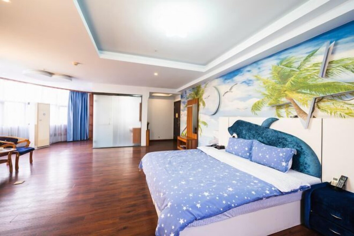 A spacious bedroom with a large bed, a mural of palm trees on the wall, and a wooden floor.