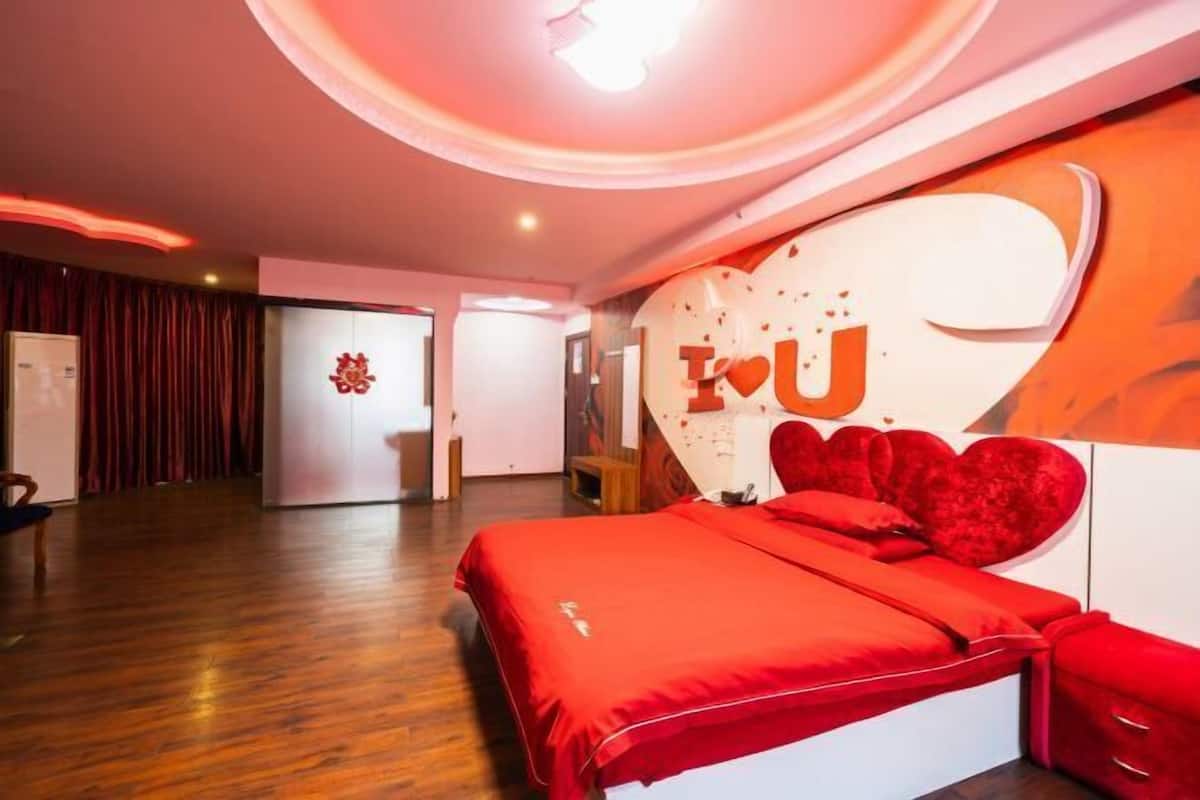 Une chambre d’hôtel moderne avec un grand lit, une tête de lit rouge et un mur orné d’un motif en forme de cœur.