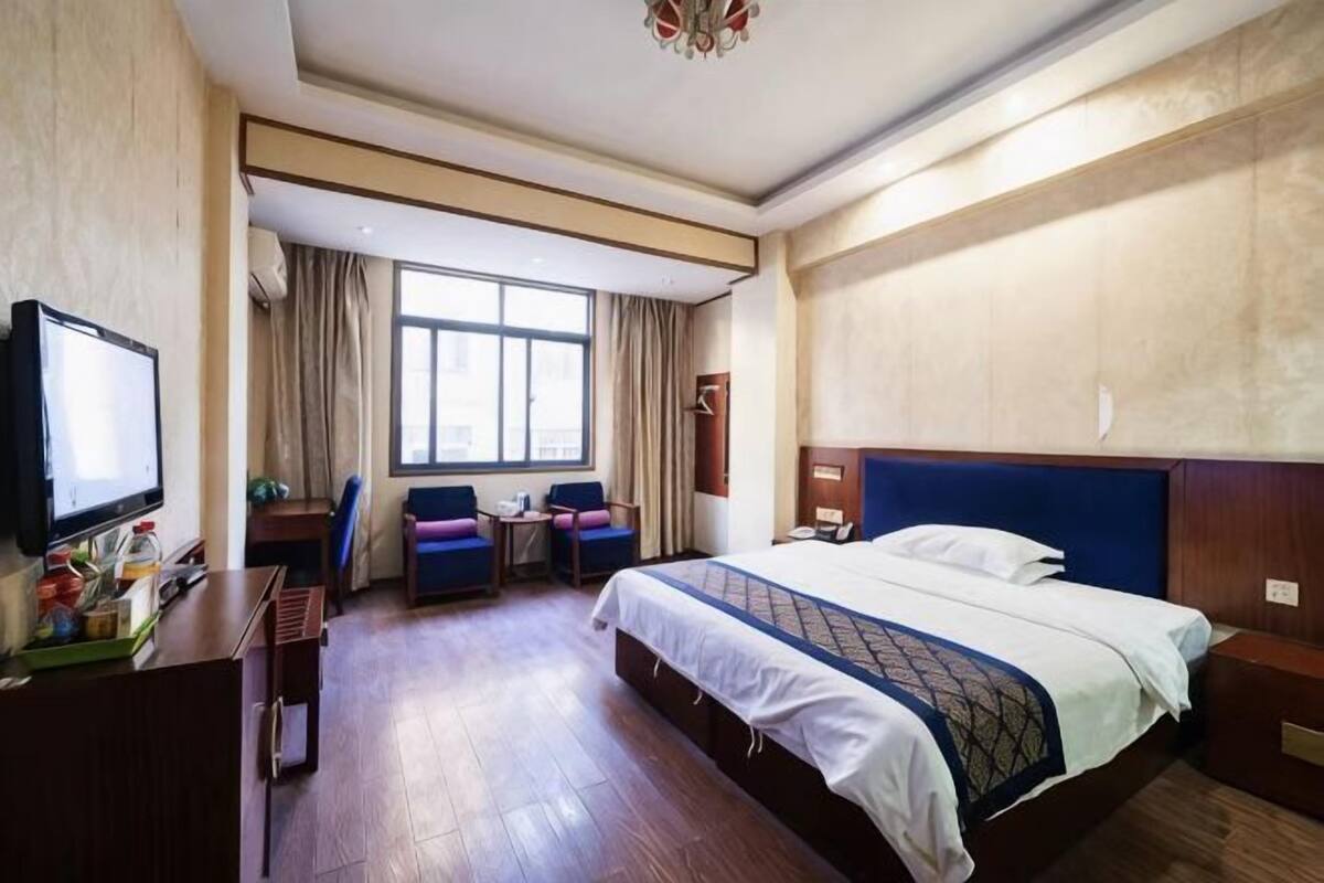 Une chambre d’hôtel avec un lit, un bureau, une chaise, une télévision et une fenêtre.