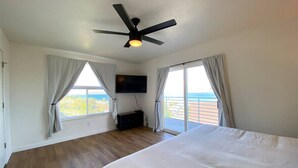 Een slaapkamer met een groot bed, een plafondventilator, een televisie en uitzicht op een balkon.