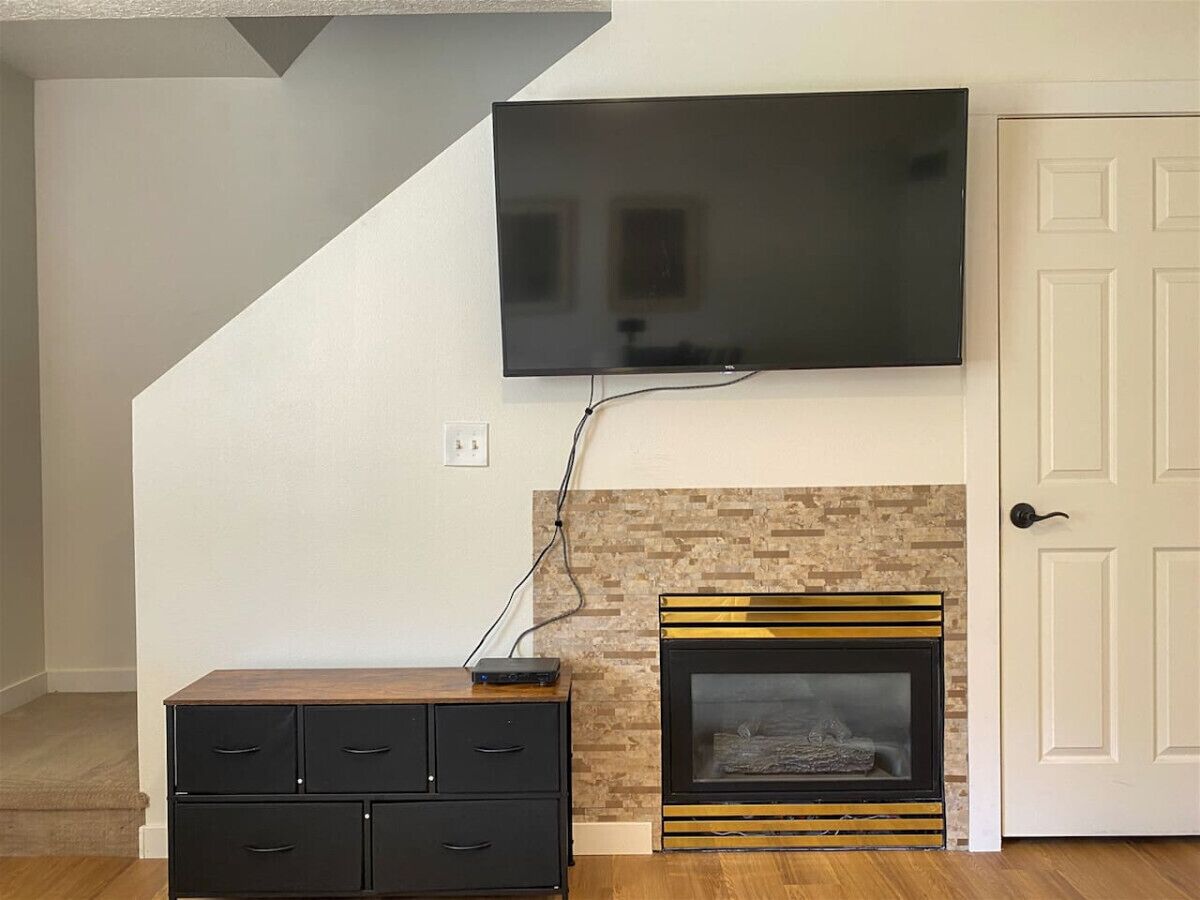 A living room with a flat-screen TV mounted on the wall, a fireplace with a gold frame, and a black entertainment unit with drawers.