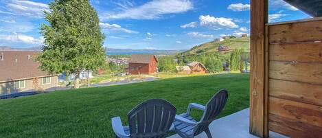 A patio with two Adirondack chairs, a wooden pergola, and a view of a green lawn and houses in the background.