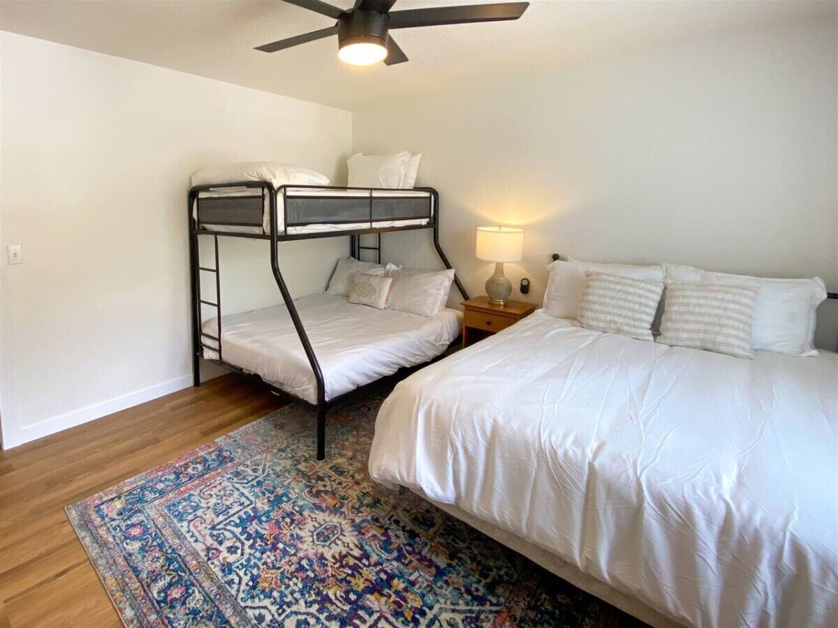 A bedroom with two bunk beds, a single bed, a patterned rug, a ceiling fan, and a bedside lamp.