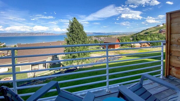 Een balkon met uitzicht op een waterpartij, een grasveld en een heuvel in de verte met huizen.
