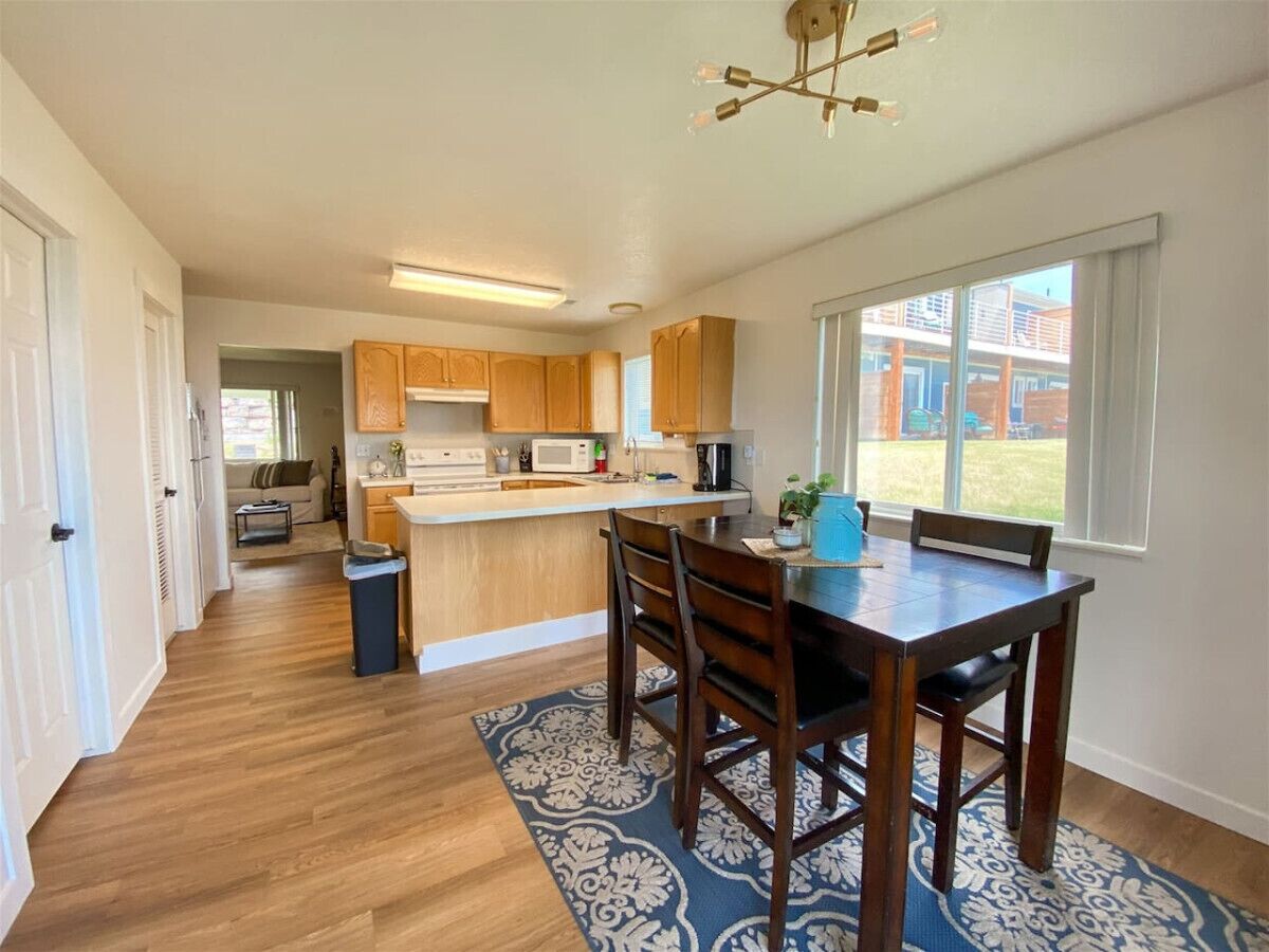 A modern kitchen with wooden cabinets, a central island, and a dining area with a table and chairs.