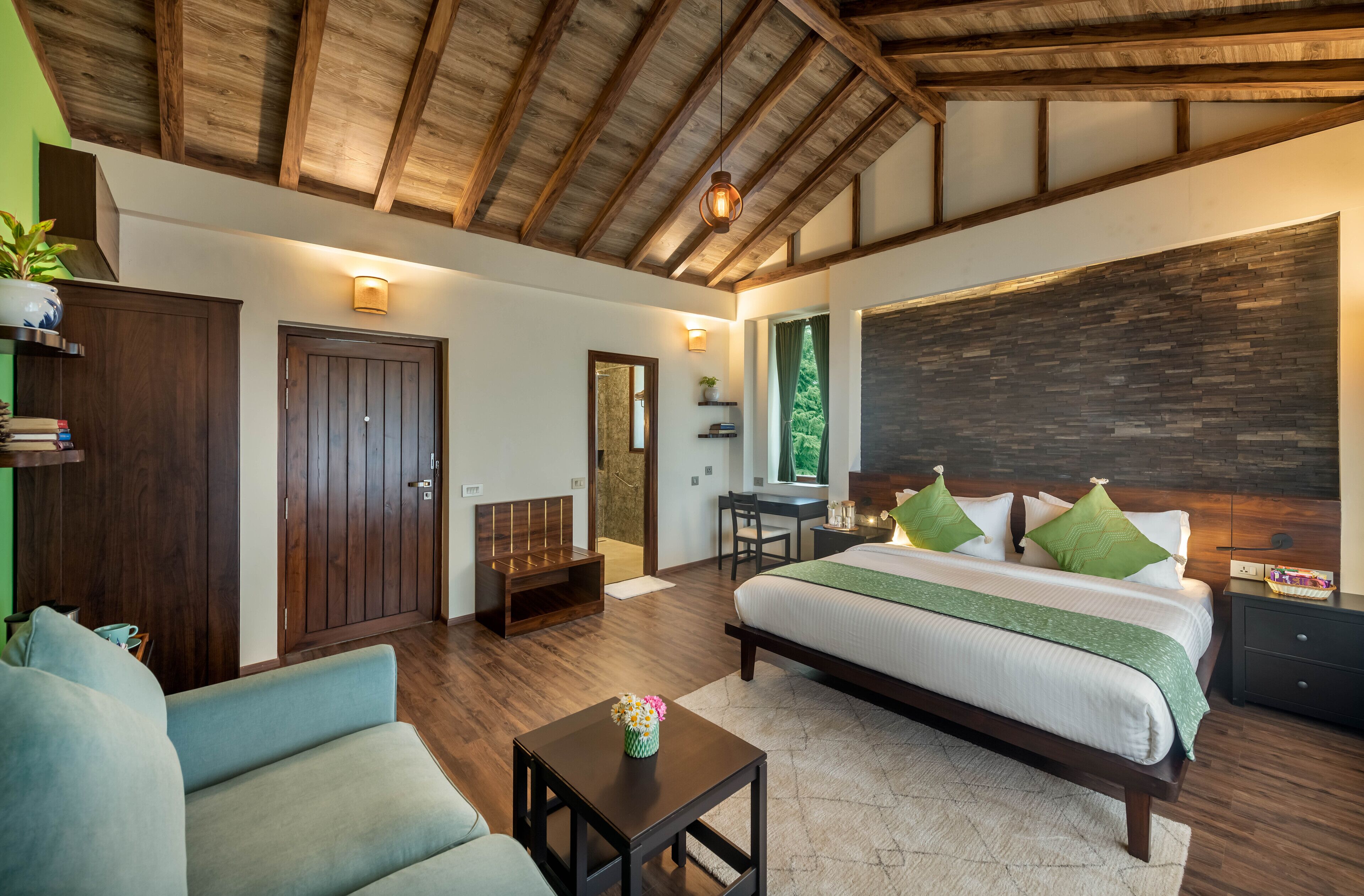 Un dormitorio con una cama grande, un escritorio y un sofá. Cuenta con techo de madera y un ventanal amplio.