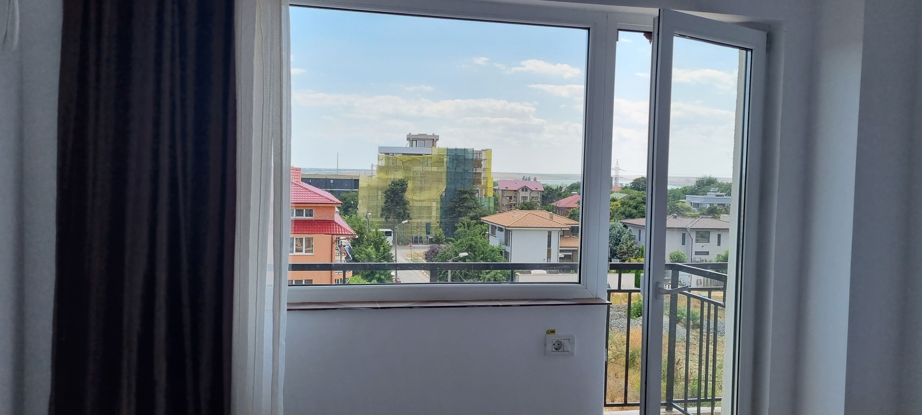 Una habitación con un ventanal amplio, pared blanca y barandilla de balcón visible.