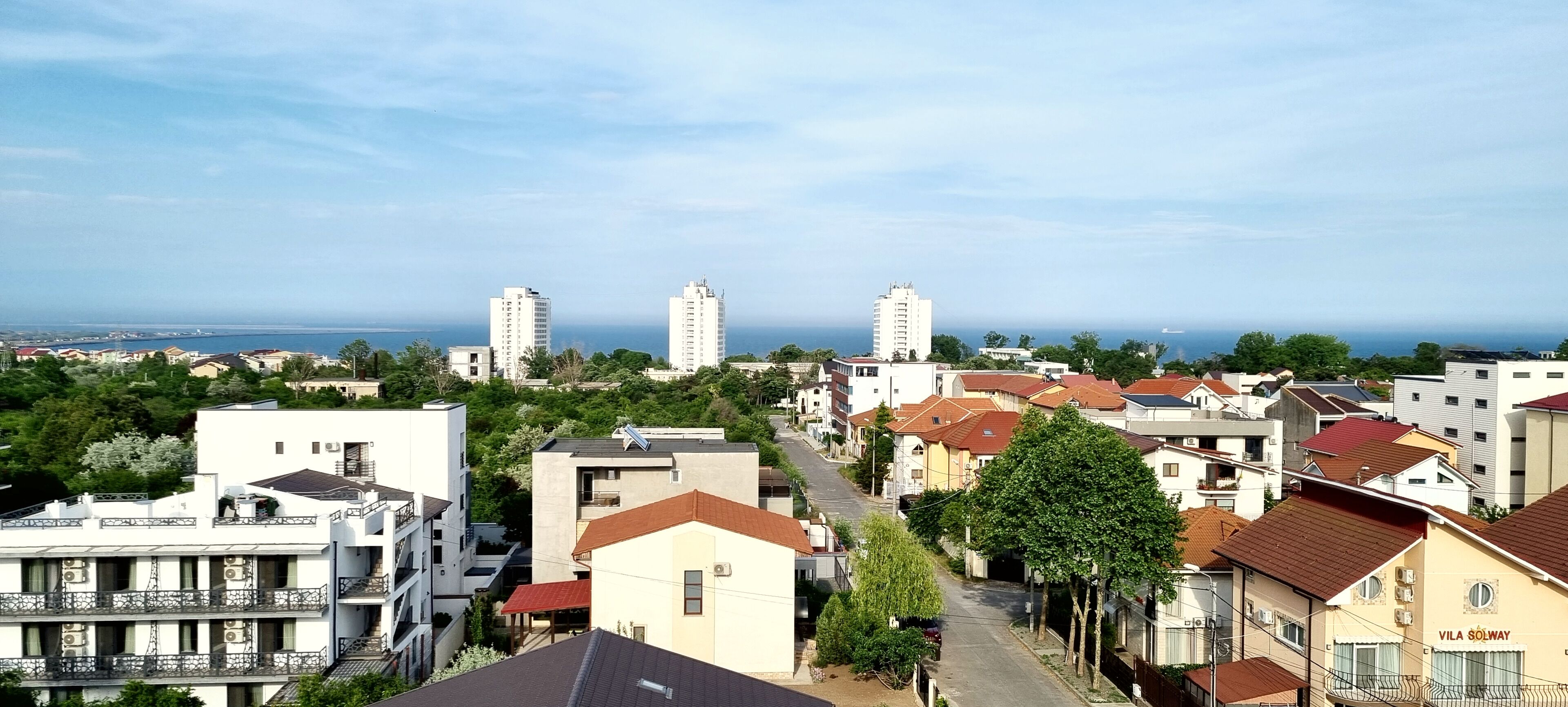 Zona residenziale caratterizzata da un mix di edifici moderni e tradizionali, con vista libera sul mare e una strada alberata.