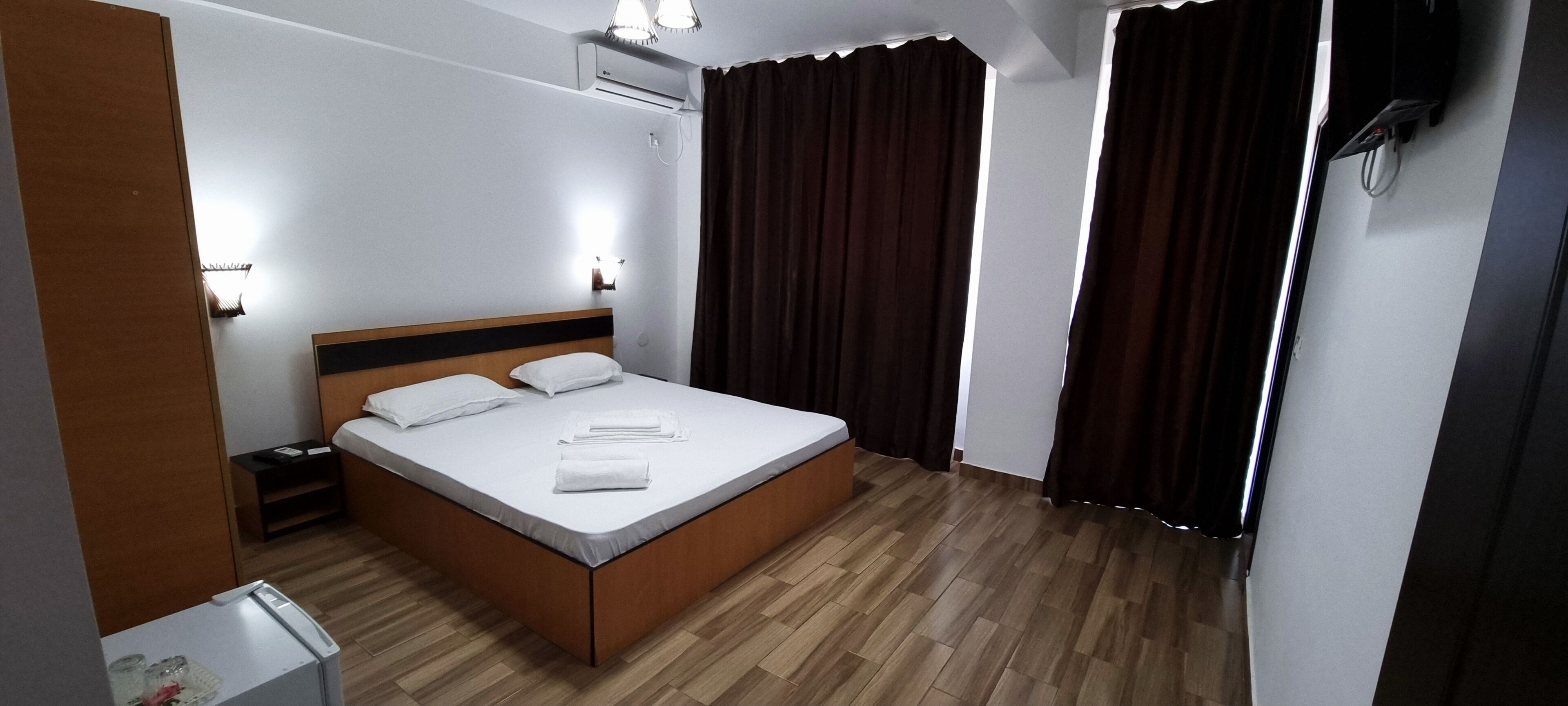 Habitación de hotel ordenada con una cama individual, mesitas de noche, un equipo de aire acondicionado y una ventana con cortinas.