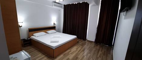 Habitación de hotel ordenada con una cama individual, mesitas de noche, un equipo de aire acondicionado y una ventana con cortinas.