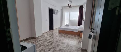 A hotel room with a bed, a TV, a window with curtains, and a tiled floor.