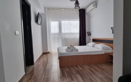 A bedroom with a wooden bed, white bedding, a TV on the wall, and a window with curtains.