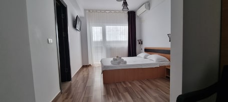A bedroom with a wooden bed, white bedding, a TV on the wall, and a window with curtains.