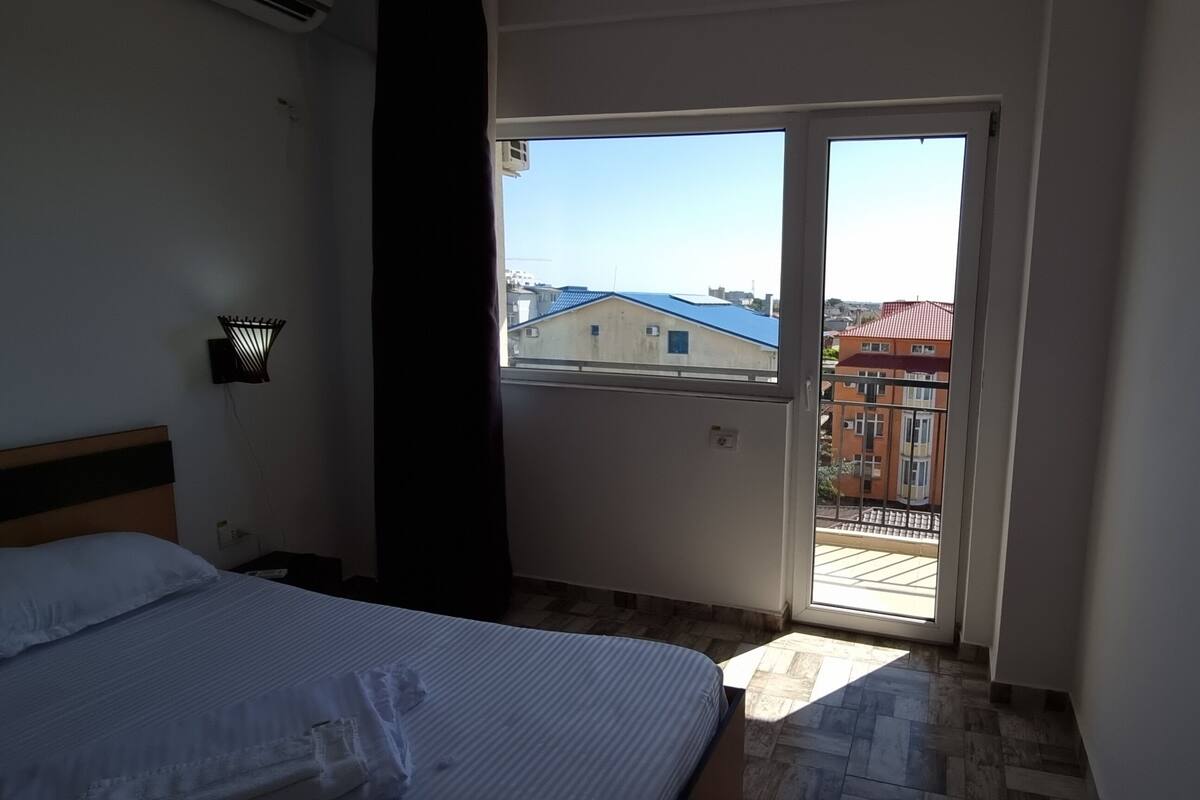 A bedroom with a bed, a nightstand, a wall-mounted lamp, and a sliding glass door leading to an outdoor balcony.