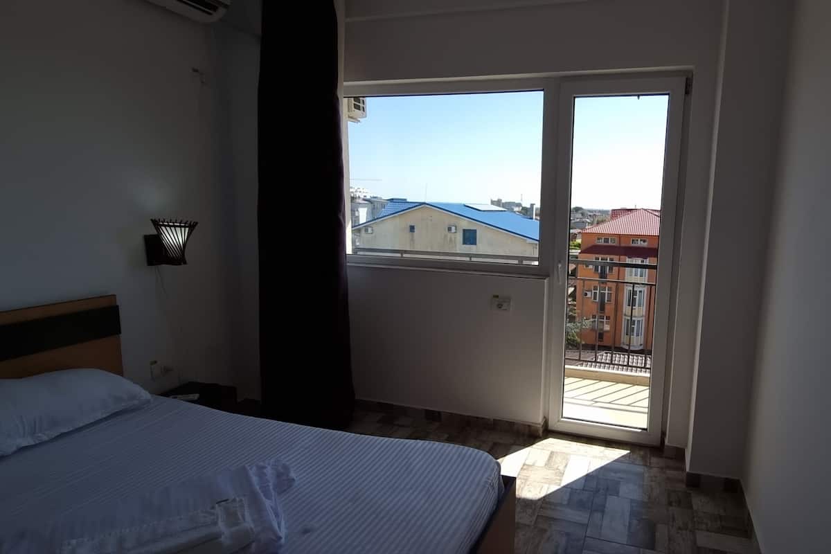 A bedroom with a bed, a nightstand, a wall-mounted lamp, and a sliding glass door leading to an outdoor balcony.
