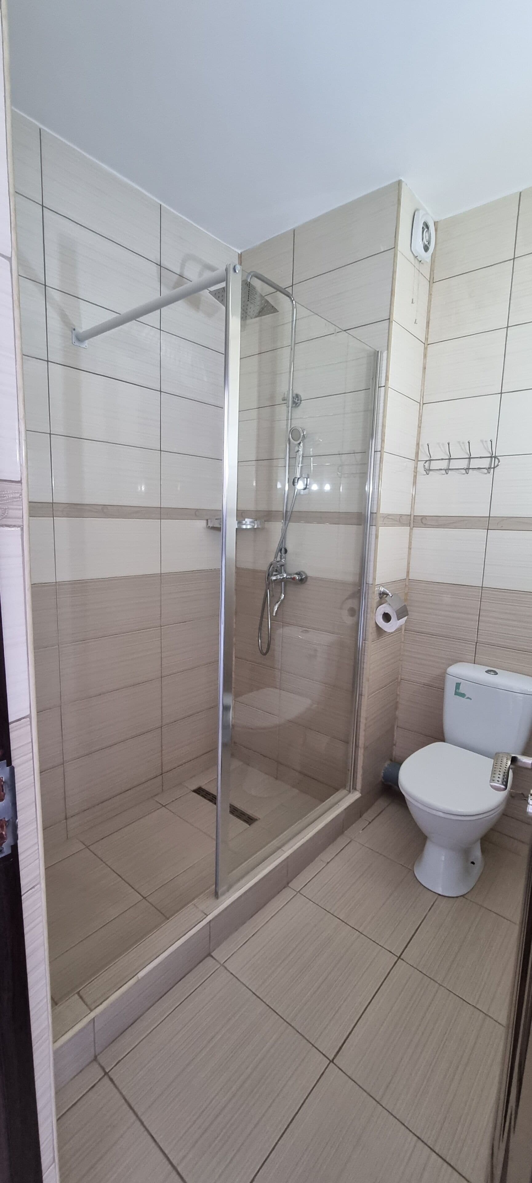 Un baño con ducha de vidrio, inodoro y toallero.
