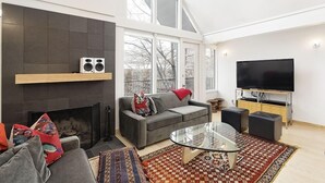 A modern living room with a fireplace, a sofa, a glass coffee table, and a television. - Fifth Avenue Unit 5 | Modern & Stylish Condo with A/C and Access to Pool & Hot Tub (Aspen)