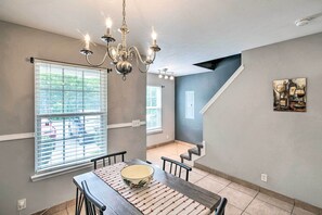 A dining area with a chandelier, a dining table with chairs, a window with blinds, and a staircase leading to another level. - La Vergne Townhome: 22 Mi to Dtwn Nashville! (La Vergne)
