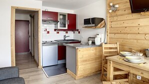 A compact kitchen with a microwave, stove, and red cabinets. There's a small dining area with a table and chairs. - Renovated studio, center, balcony, 3 pers., 5th floor (Les Menuires)