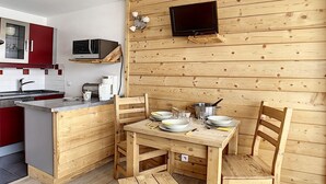 A compact kitchen with a wooden wall, a microwave, a sink, and a dining area with chairs and a table. - Renovated studio, center, balcony, 3 pers., 5th floor (Les Menuires)