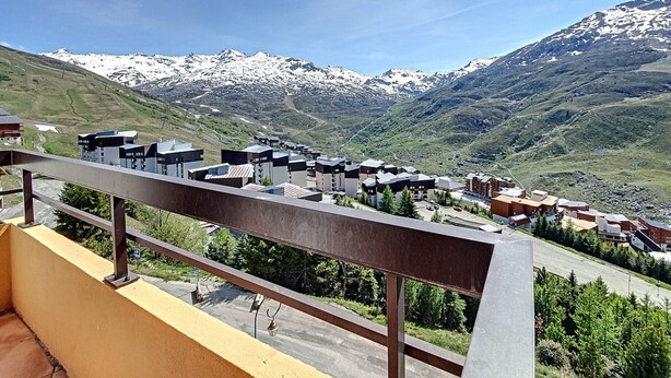 A mountain resort with modern buildings, a paved road, and snow-capped peaks in the background.
