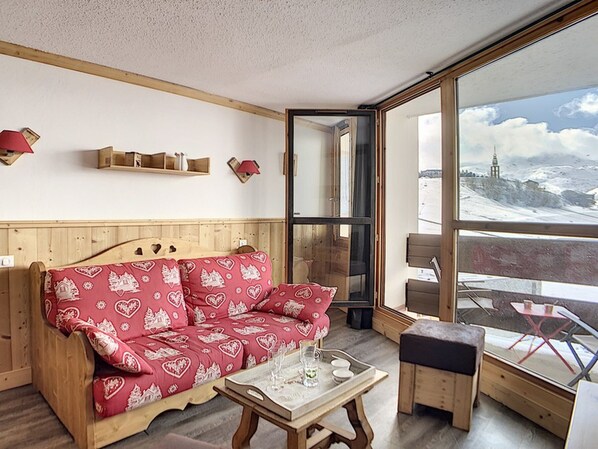 Een gezellige kamer met een houten bank, een klein tafeltje en uitzicht op een besneeerd landschap door grote ramen.