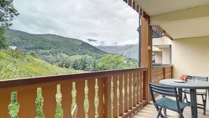 A balcony with a wooden railing, a table with chairs, and a view of green hills and mountains. - Spacious apartment for 10, balcony, parking, near slopes (Saint-Martin-de-Belleville)