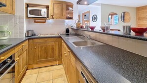 A modern kitchen with wooden cabinets, a microwave, a sink, and a dishwasher. - Spacious apartment for 10, balcony, parking, near slopes (Saint-Martin-de-Belleville)