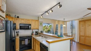 Eine moderne Küche mit Holzausstattung, einem schwarzen Kühlschrank, einer Mikrowelle, einem Backofen und einem Geschirrspüler. Eine große Kücheninsel mit Spüle und Pendelleuchte darüber.
