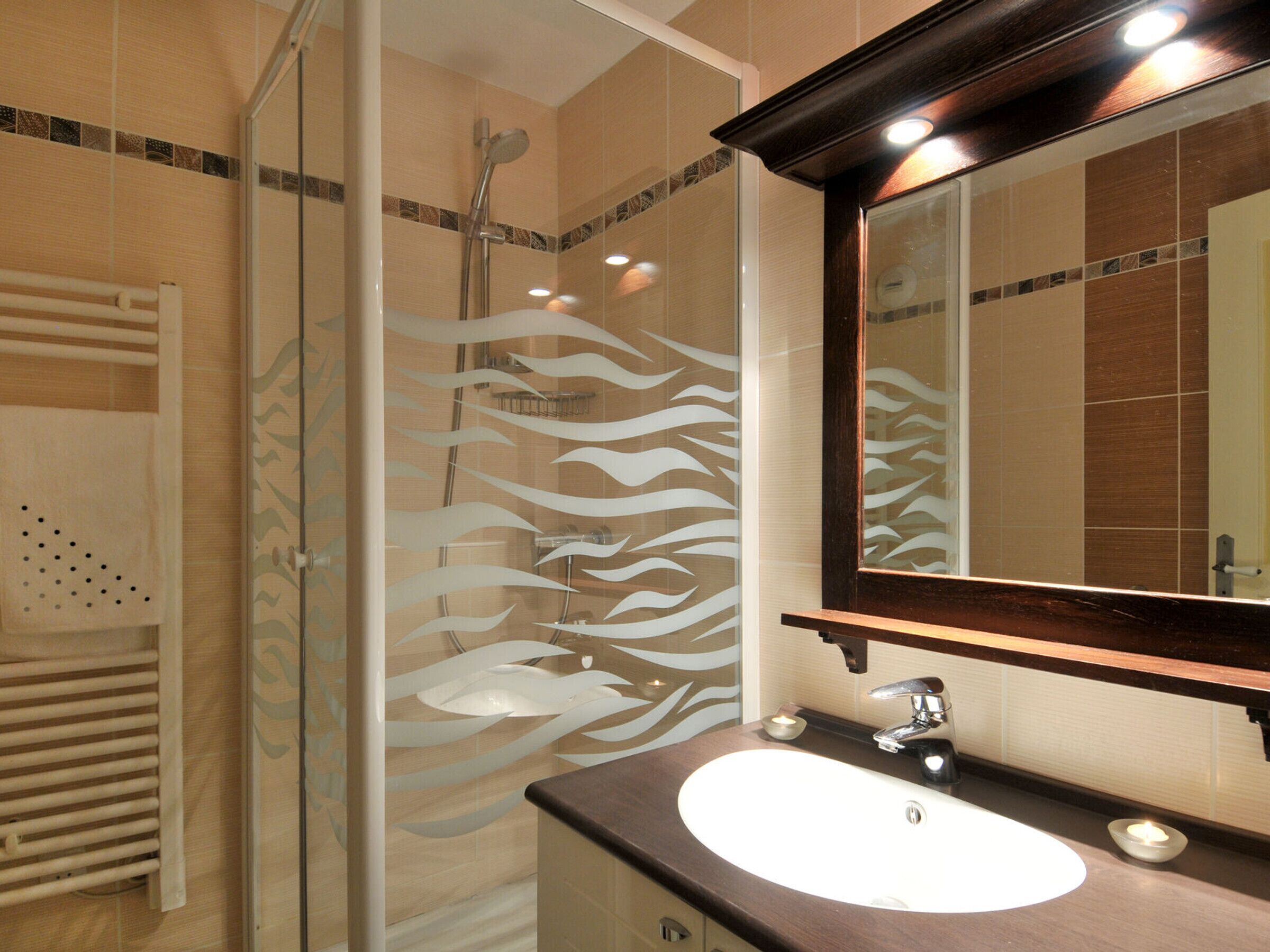 Une salle de bain avec une douche à parois de verre, un lavabo blanc et un miroir avec un cadre en bois.