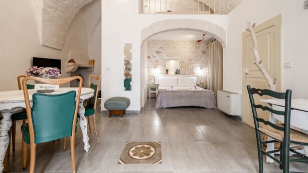 Un comedor con techo alto, paredes de piedra y vistas a un dormitorio con cama y cortinas.