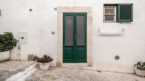 Un edificio blanco con una puerta verde, una ventana con contraventanas y plantas en macetas.