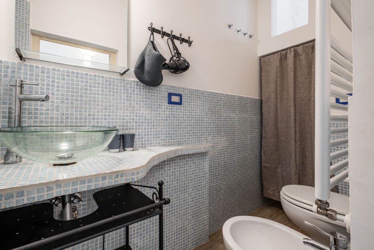A bathroom with a glass basin, a towel rack, a toilet, and a shower curtain.