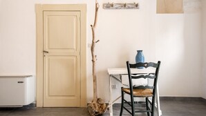 Una habitación con una puerta doble, un pequeño electrodoméstico blanco, una rama rústica, una mesa blanca con un jarrón azul y una silla negra.