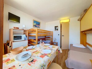 A compact room with bunk beds, a dining table set for two, a microwave, and a television. - Studio at the slopes with balcony (Les Menuires)