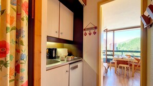 A compact kitchen with a coffee maker, a toaster, and a sink. There is a wooden door leading to a balcony with a table and chairs.