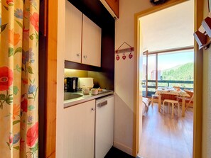 A compact kitchen with a coffee maker, a toaster, and a sink. There is a wooden door leading to a balcony with a table and chairs. - Studio at the slopes with balcony (Les Menuires)