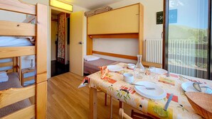 A compact room with bunk beds, a dining table set for two, and a view of a balcony.